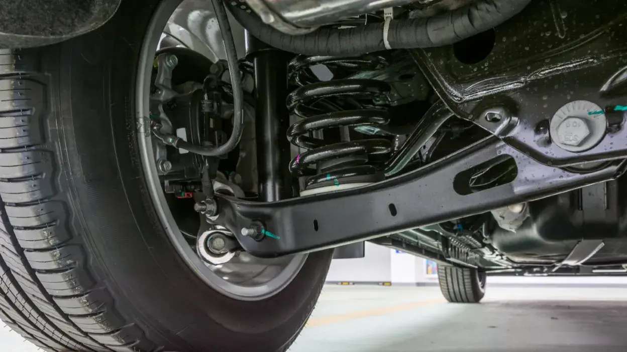 Vista detalhada da suspensão e amortecedor de um veículo, incluindo mola helicoidal e braço de controlo.