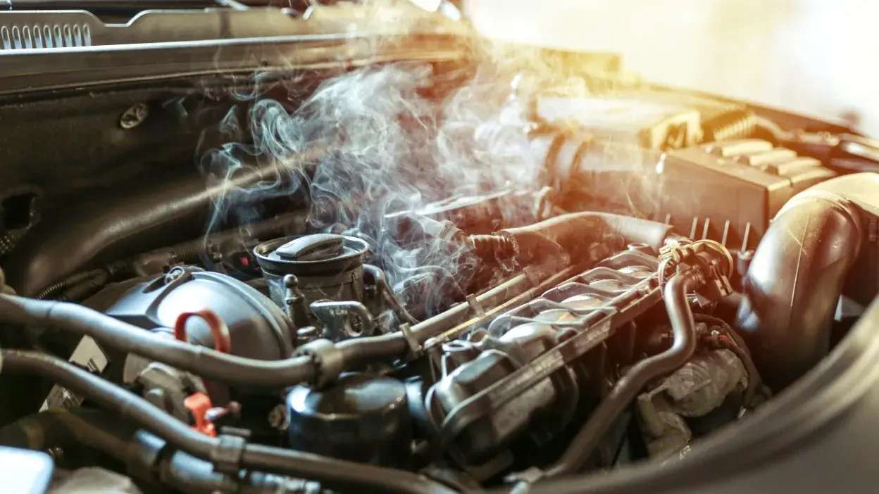 Motor de carro com fumo a sair, indicando possível sobreaquecimento.